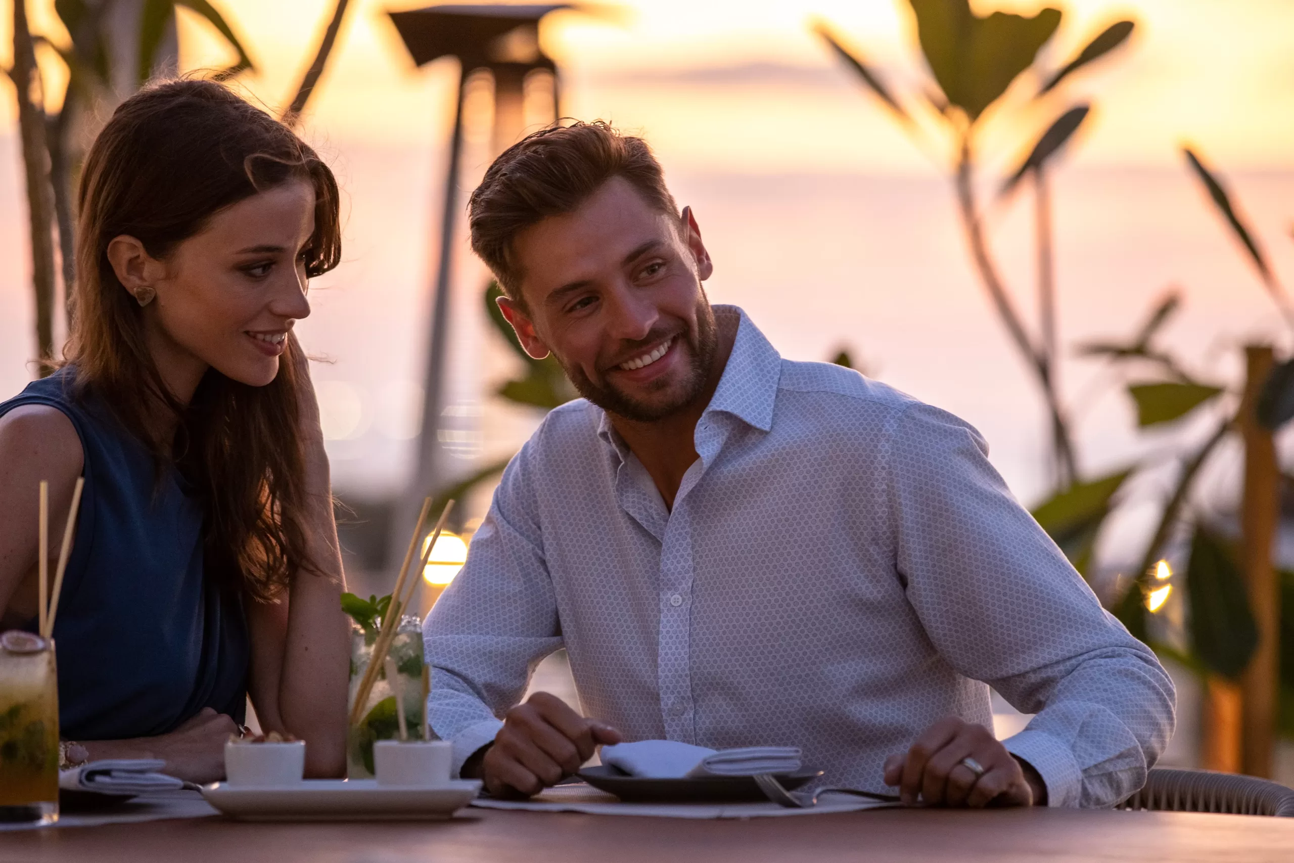 A couple smiling at dinner as the sun sets at Jumeirah Saadiyat Island